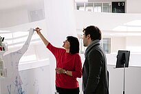 Zwei Leute stehen vor einem Whiteboard und schreiben darauf