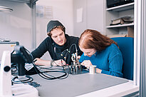 A female student works on a machine while a male student observes